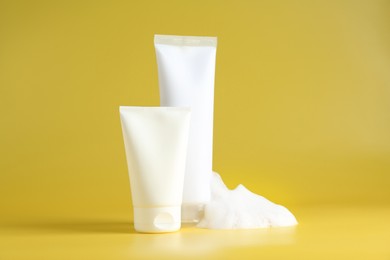 Tubes of cosmetic products with foam on yellow background