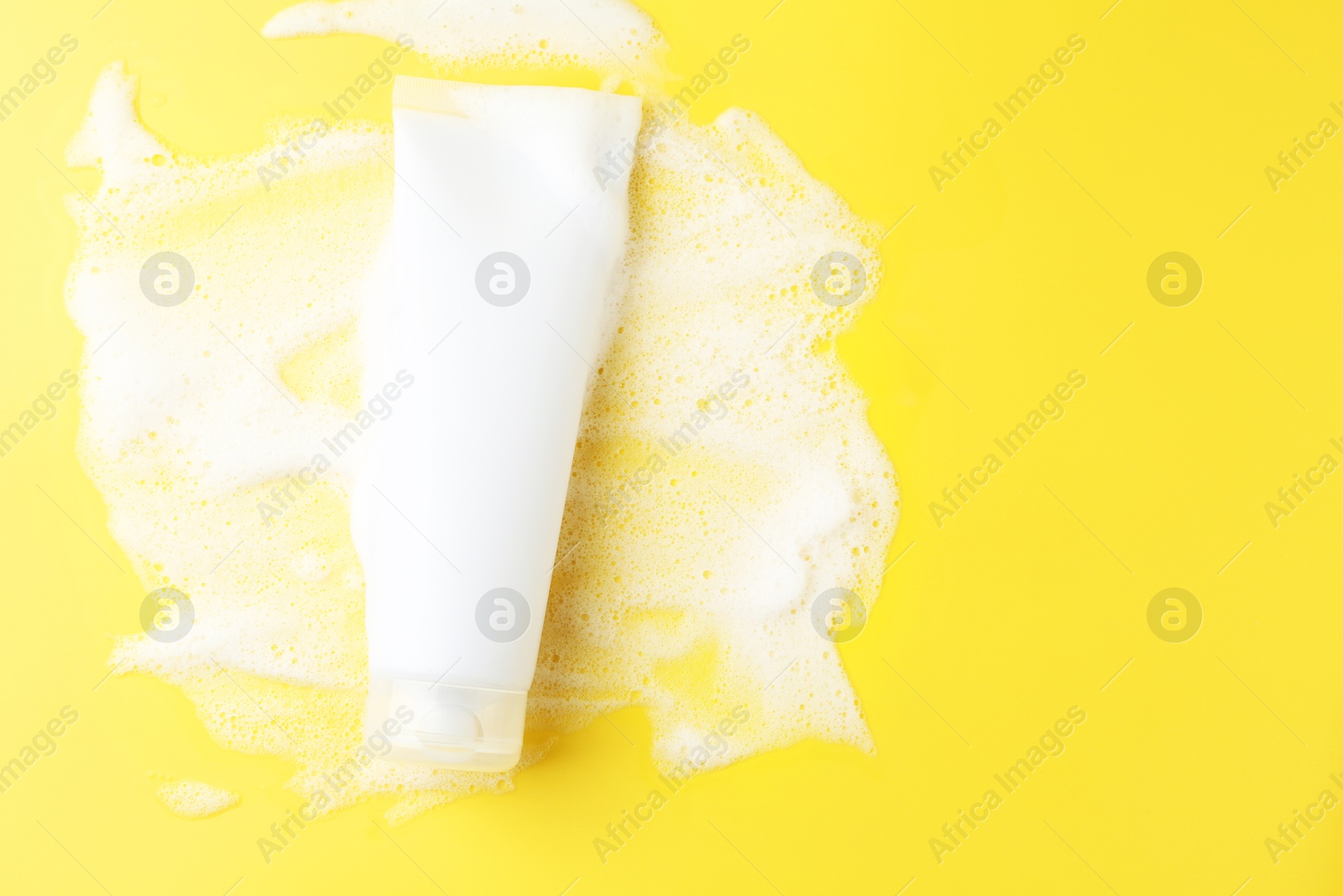 Photo of Tube of cosmetic product with foam on yellow background, top view