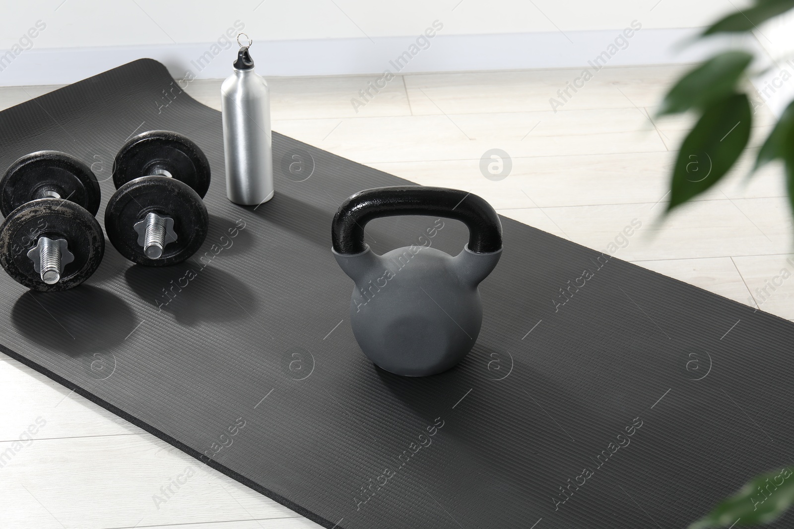 Photo of Kettlebell, barbells, thermo bottle and mat on floor indoors