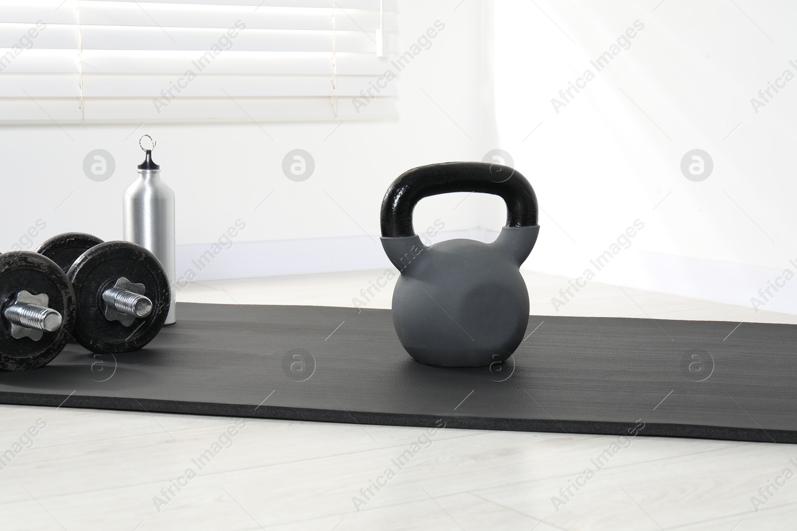 Photo of Kettlebell, barbells, thermo bottle and mat on floor indoors