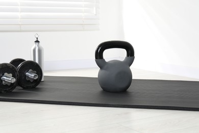 Photo of Kettlebell, barbells, thermo bottle and mat on floor indoors