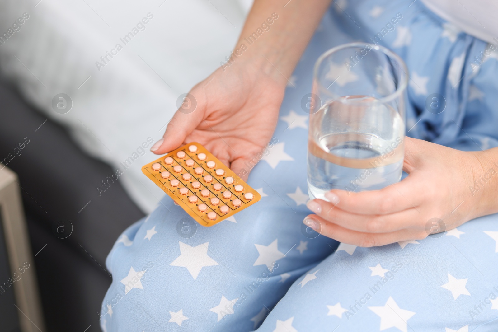 Photo of Woman with contraceptive pills and glass of water on bed, closeup