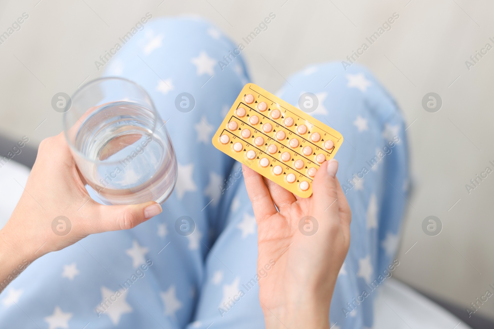 Photo of Woman with contraceptive pills and glass of water indoors, above view