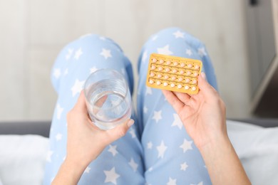 Photo of Woman with contraceptive pills and glass of water on bed, above view