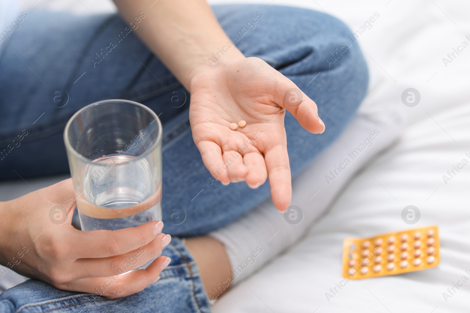 Photo of Woman with contraceptive pills and glass of water on bed, closeup