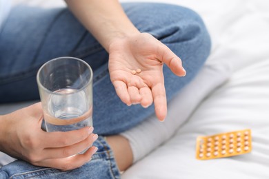 Photo of Woman with contraceptive pills and glass of water on bed, closeup