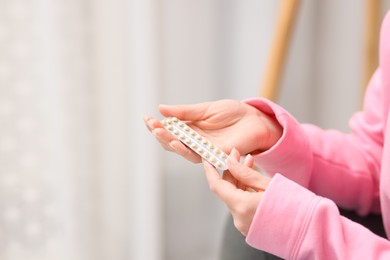 Photo of Woman with blister of contraceptive pills indoors, closeup. Space for text