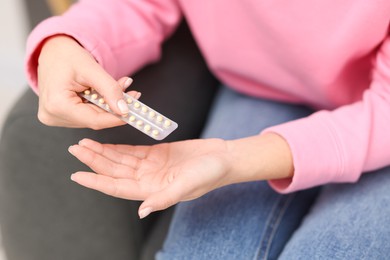 Photo of Woman taking contraceptive pill out from blister indoors, closeup