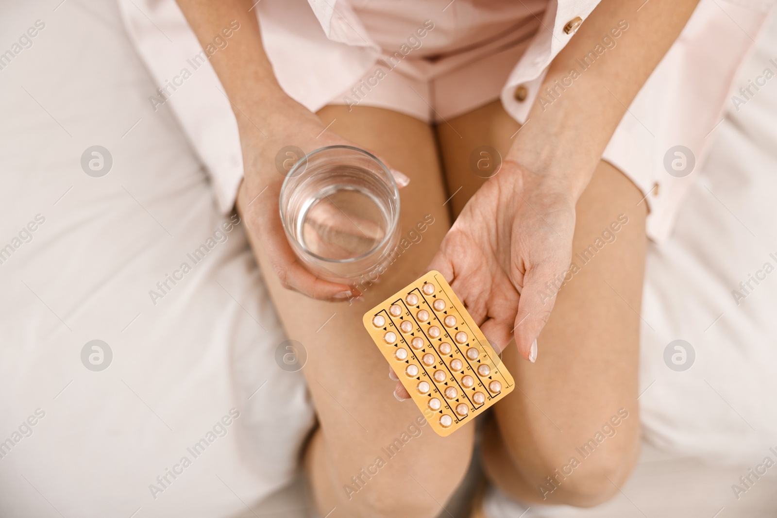 Photo of Woman with contraceptive pills and glass of water on bed, top view