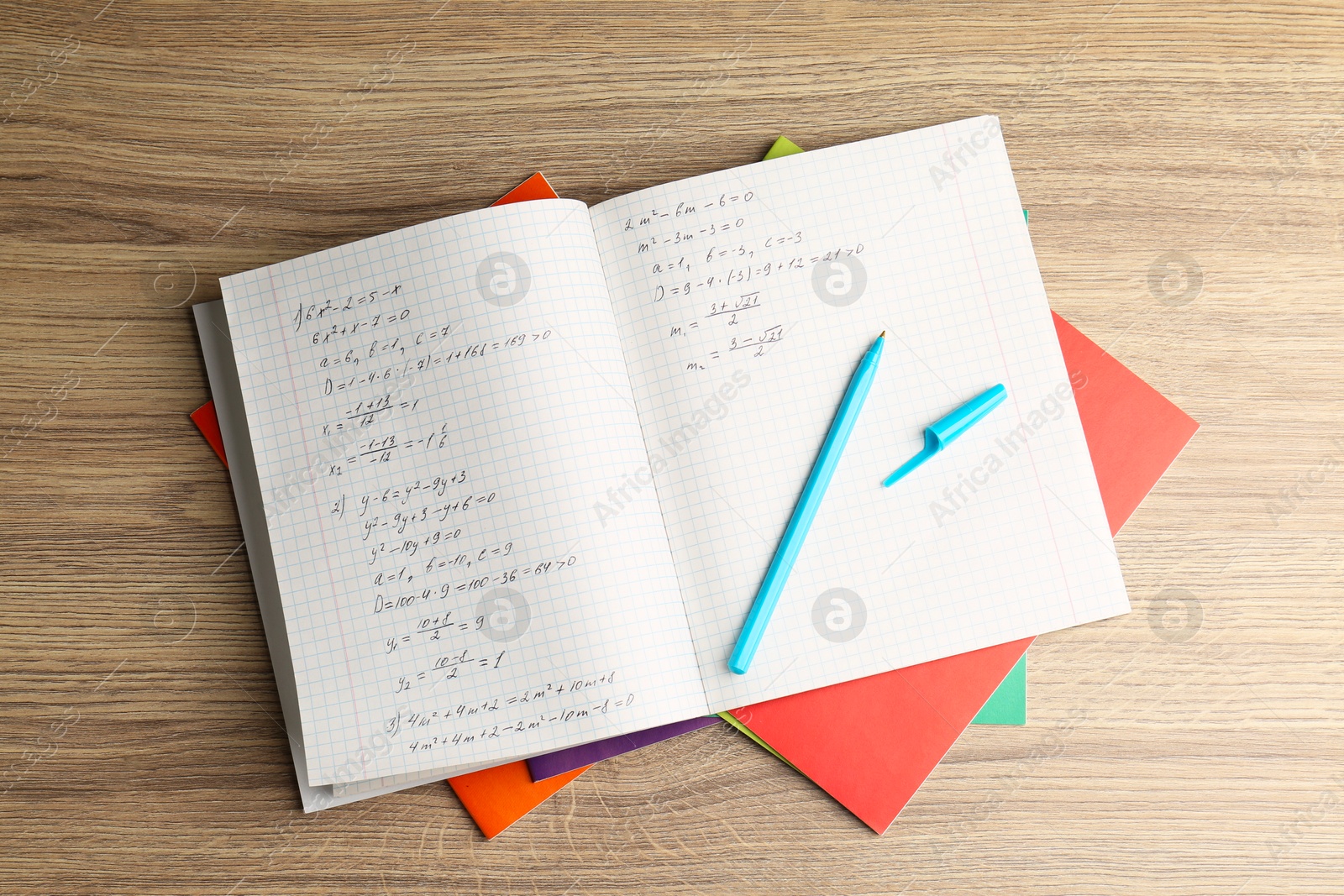 Photo of Doing homework. Copybook with math assignment and stationery on wooden table, top view