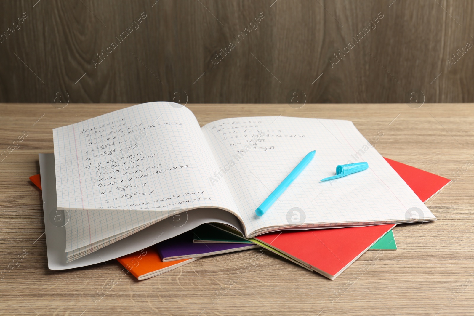 Photo of Doing homework. Copybook with math assignment and stationery on wooden table, closeup