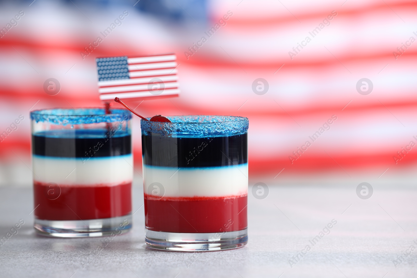 Tasty cocktails in glasses with small paper flag of USA on table against blurred background, space for text Photo of Tasty cocktails in glasses with small paper flag of USA on table against blurred background, space for text