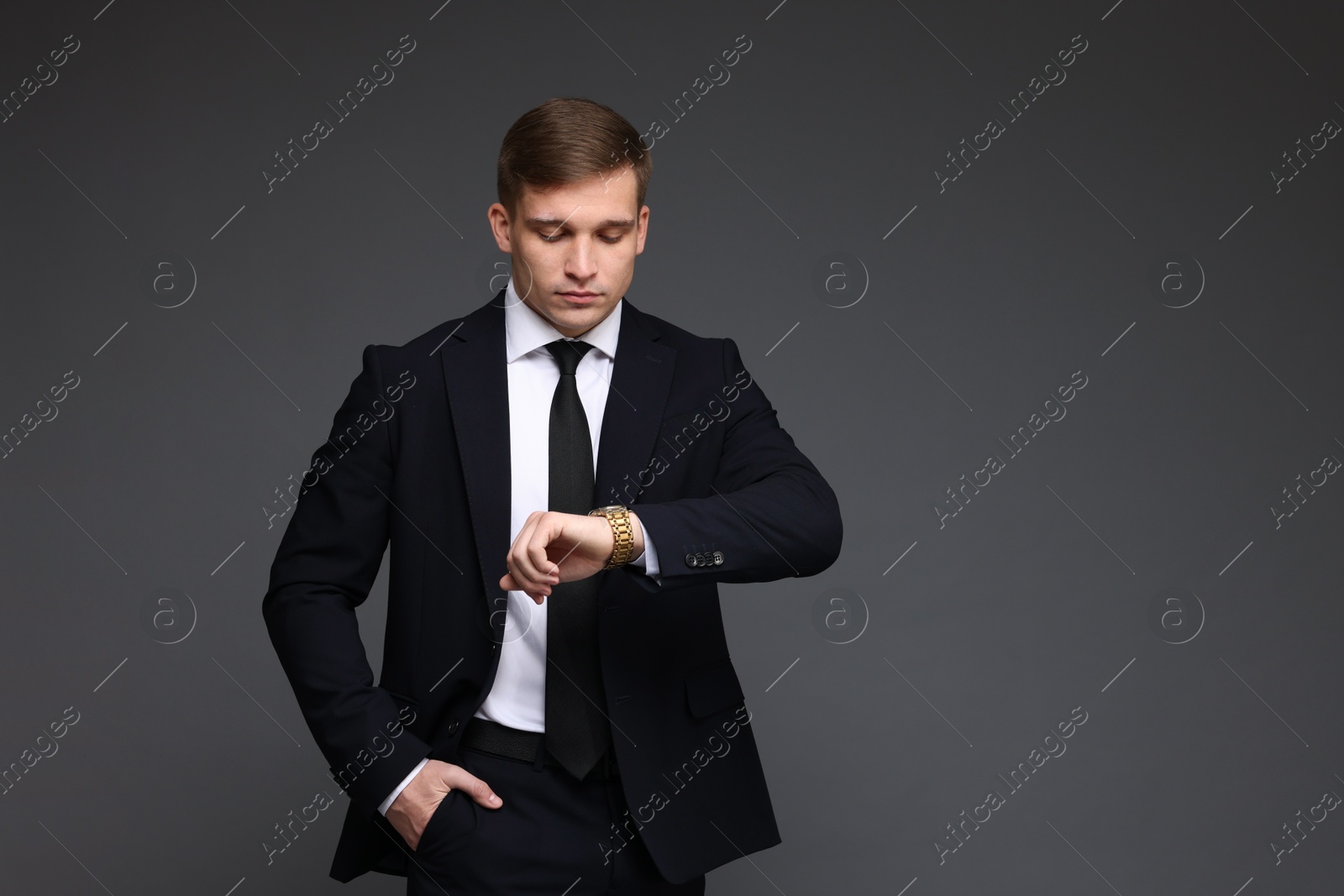 Photo of Man in classic suit checking time on grey background. Space for text