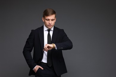 Photo of Man in classic suit checking time on grey background. Space for text