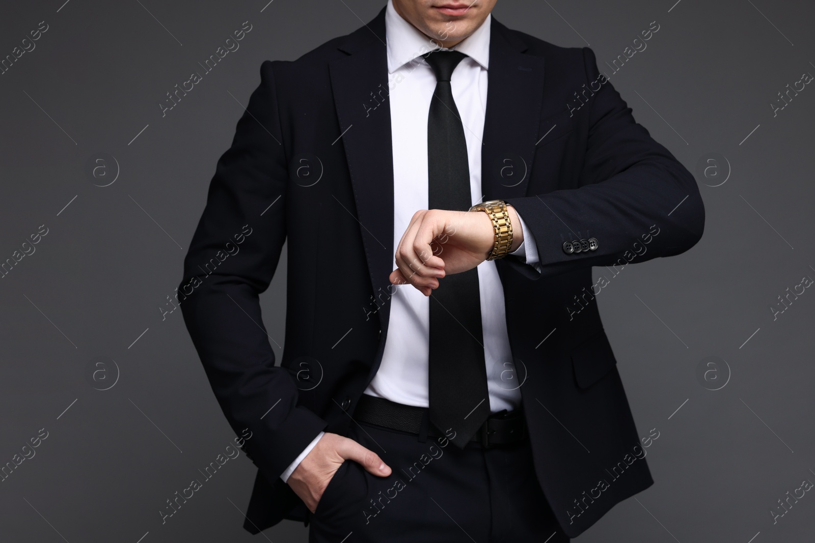 Photo of Man in classic suit checking time on grey background, closeup