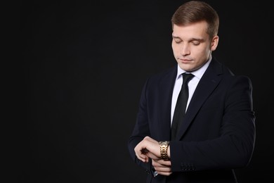 Photo of Man in classic suit checking time on black background. Space for text