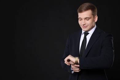 Photo of Man in classic suit checking time on black background. Space for text