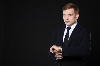 Man in classic suit with stylish watch on black background. Space for text