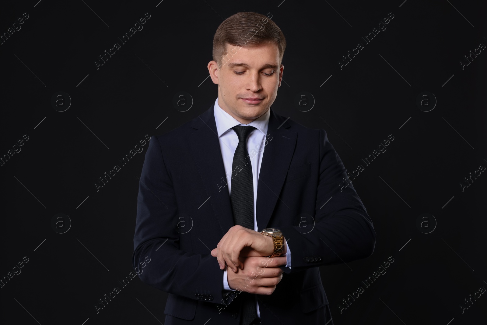 Photo of Man in classic suit checking time on black background