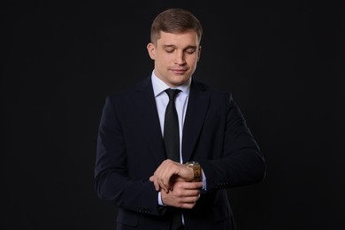 Photo of Man in classic suit checking time on black background