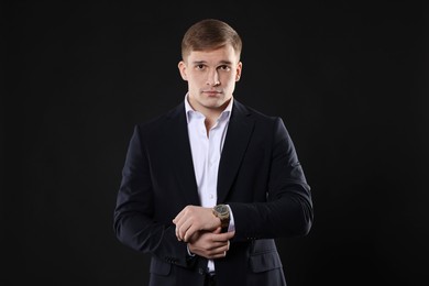 Man in classic suit with stylish watch on black background