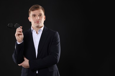 Man in classic suit with glasses on black background. Space for text