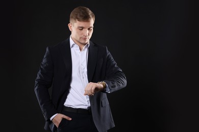 Photo of Man in classic suit checking time on black background. Space for text