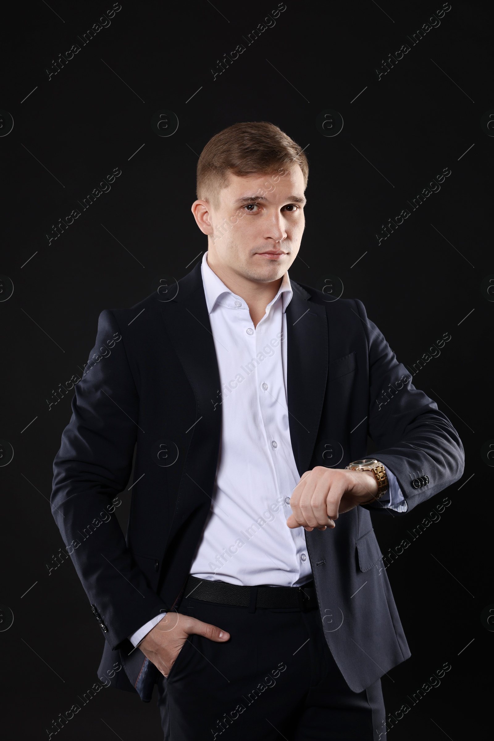 Photo of Man in classic suit checking time on black background