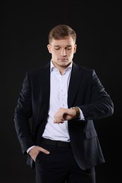 Man in classic suit checking time on black background