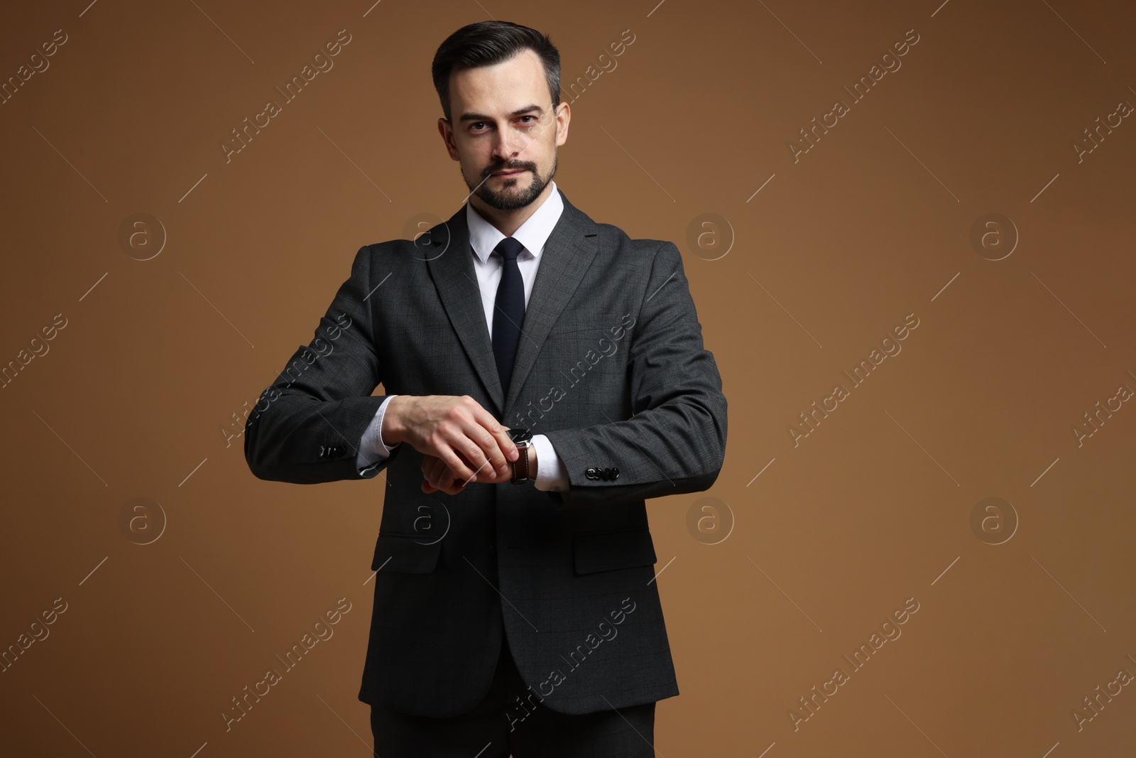 Photo of Man in classic suit checking time on brown background