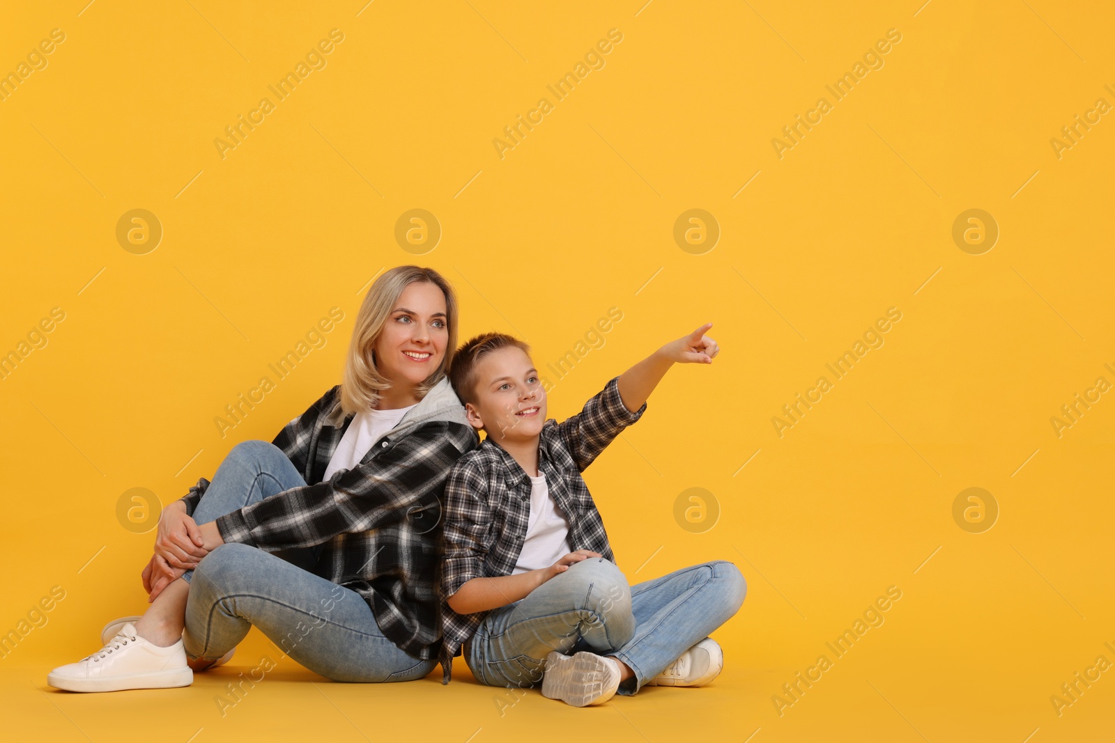 Photo of Son showing his mother something on orange background. Space for text