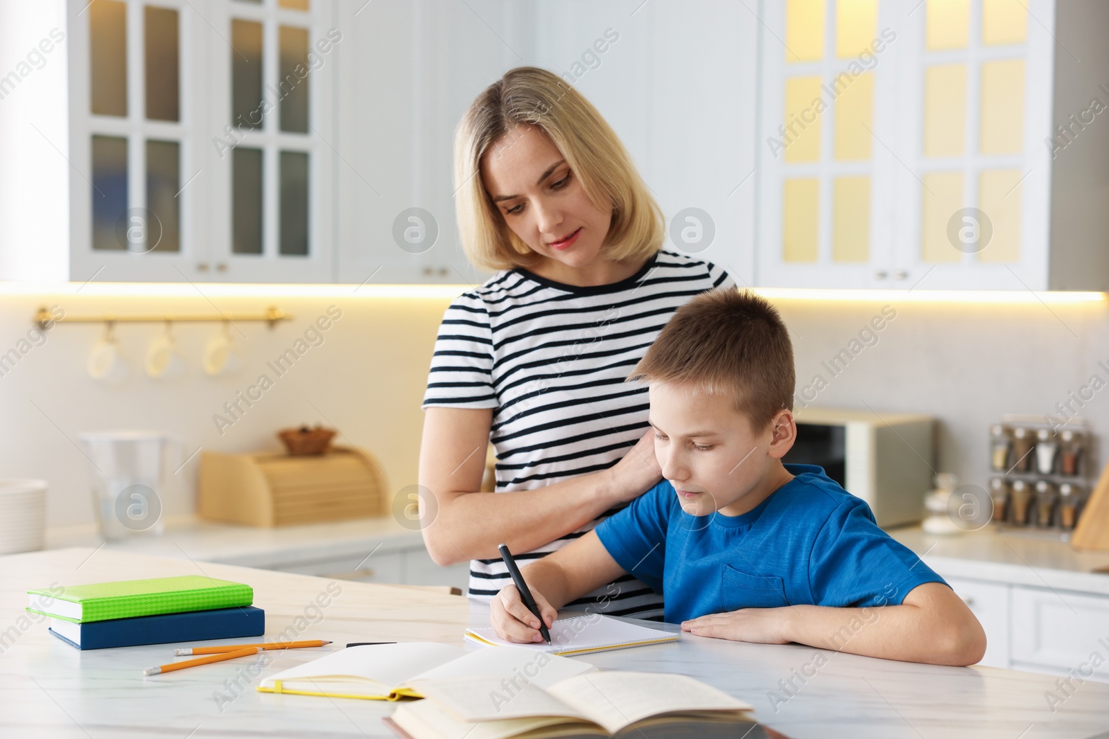 Photo of Mother and son doing homework at table indoors