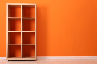 Photo of Empty wooden shelving unit near orange wall indoors, space for text