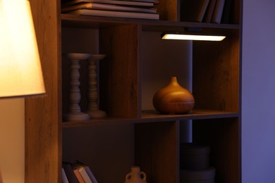 Photo of Wooden shelving unit with books and air humidifier near color wall, closeup