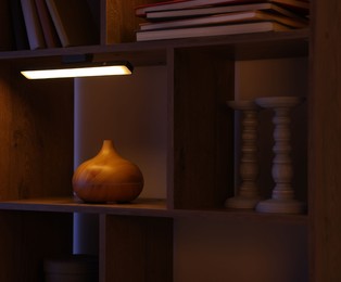 Photo of Wooden shelving unit with books and air humidifier near color wall, closeup