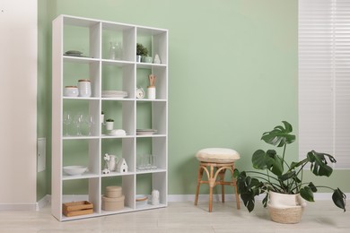 Photo of Shelving unit with dishware near olive wall indoors. Space for text