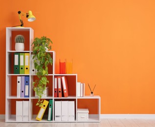 Photo of Shelving unit with folders and plants near orange wall indoors. Space for text