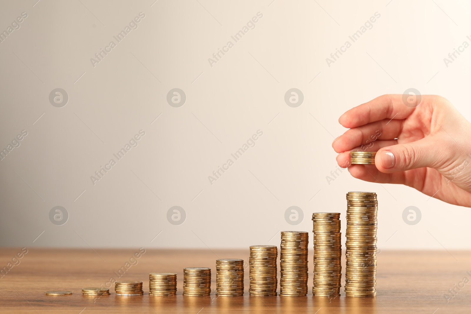 Woman putting coins onto stacks of ones at wooden table against grey background, closeup. Space for text Photo of Woman putting coins onto stacks of ones at wooden table against grey background, closeup. Space for text