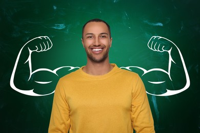 Image of Happy man with drawing of strong arms behind him on green chalkboard