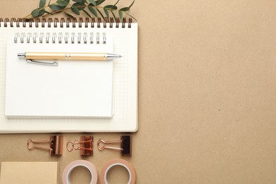 Photo of Binder clips, other stationery and green branches on beige background, flat lay. Space for text