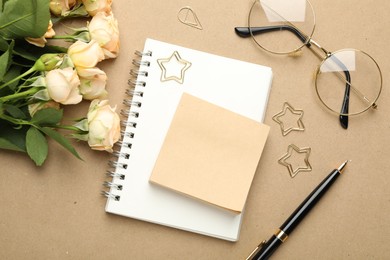 Photo of Paper clips, other stationery, glasses and roses on beige background, flat lay