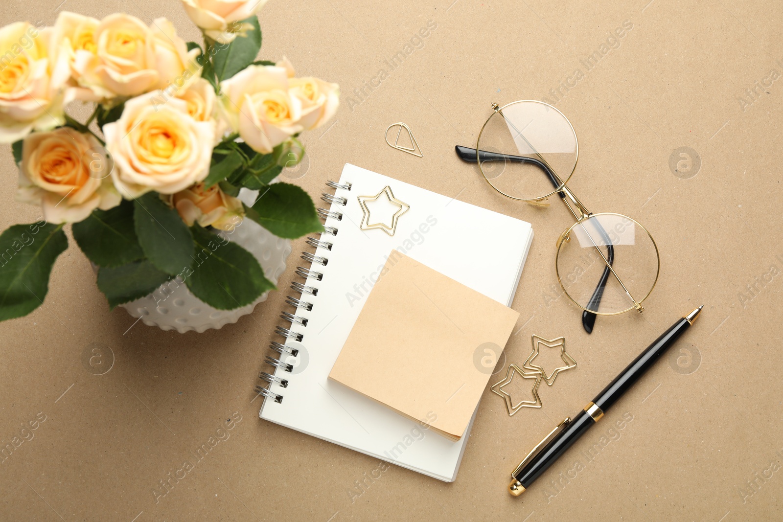 Photo of Paper clips, other stationery, glasses and roses on beige background, flat lay