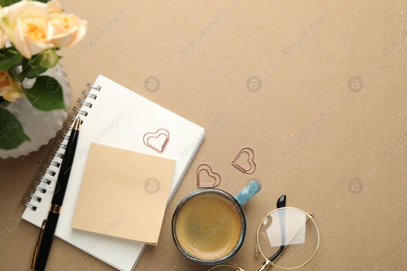 Photo of Paper clips, other stationery, coffee and roses on beige background, flat lay. Space for text