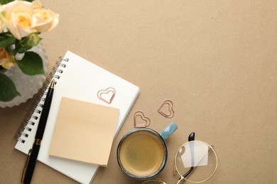 Photo of Paper clips, other stationery, coffee and roses on beige background, flat lay. Space for text