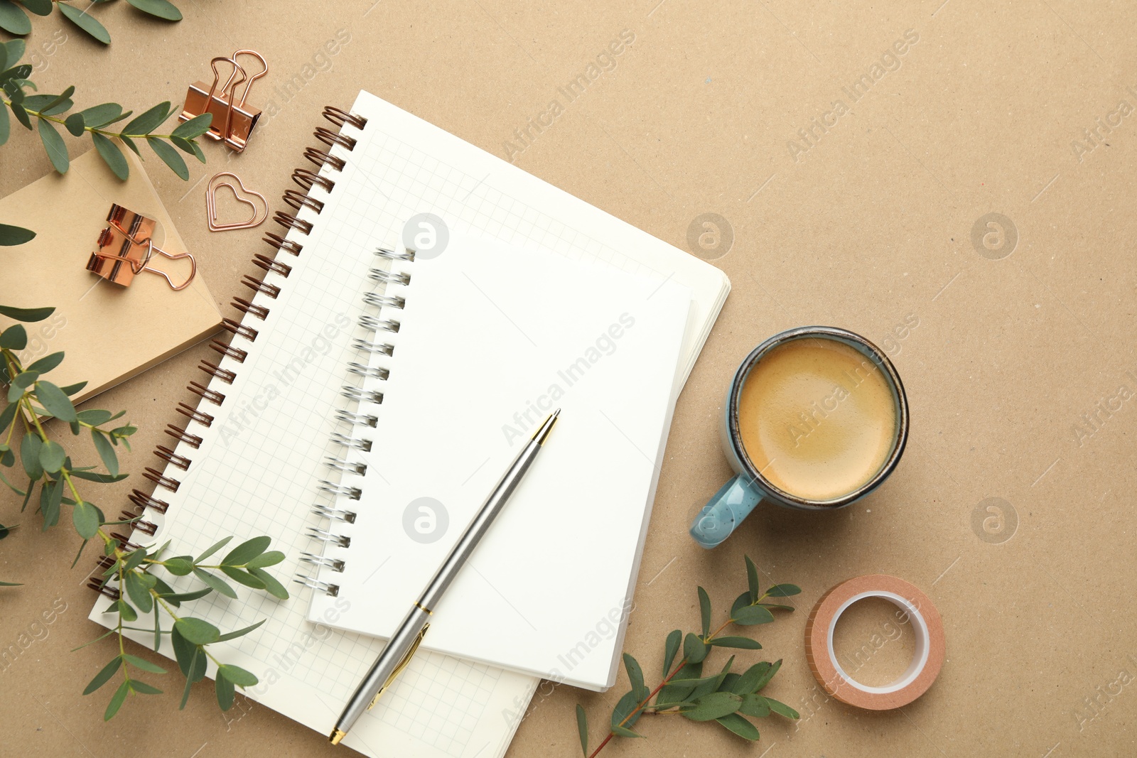 Photo of Binder clips, other stationery, coffee and green branches on beige background, flat lay