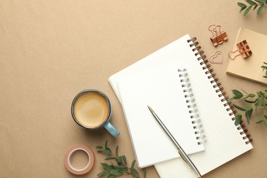 Photo of Binder clips, other stationery, coffee and green branches on beige background, flat lay. Space for text