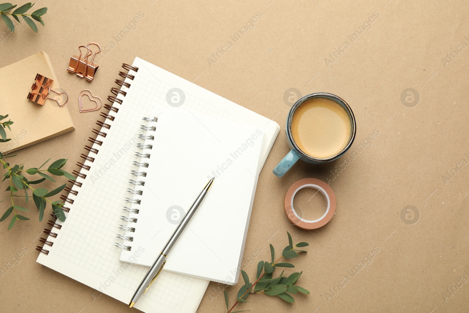 Photo of Binder clips, other stationery, coffee and green branches on beige background, flat lay. Space for text