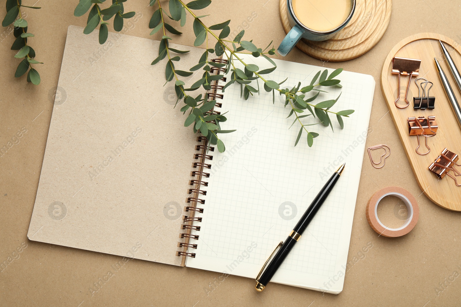 Photo of Binder clips, other stationery, coffee and green branches on beige background, flat lay