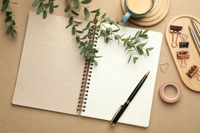 Binder clips, other stationery, coffee and green branches on beige background, flat lay