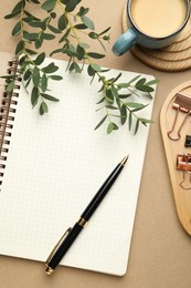 Photo of Binder clips, other stationery, coffee and green branches on beige background, flat lay